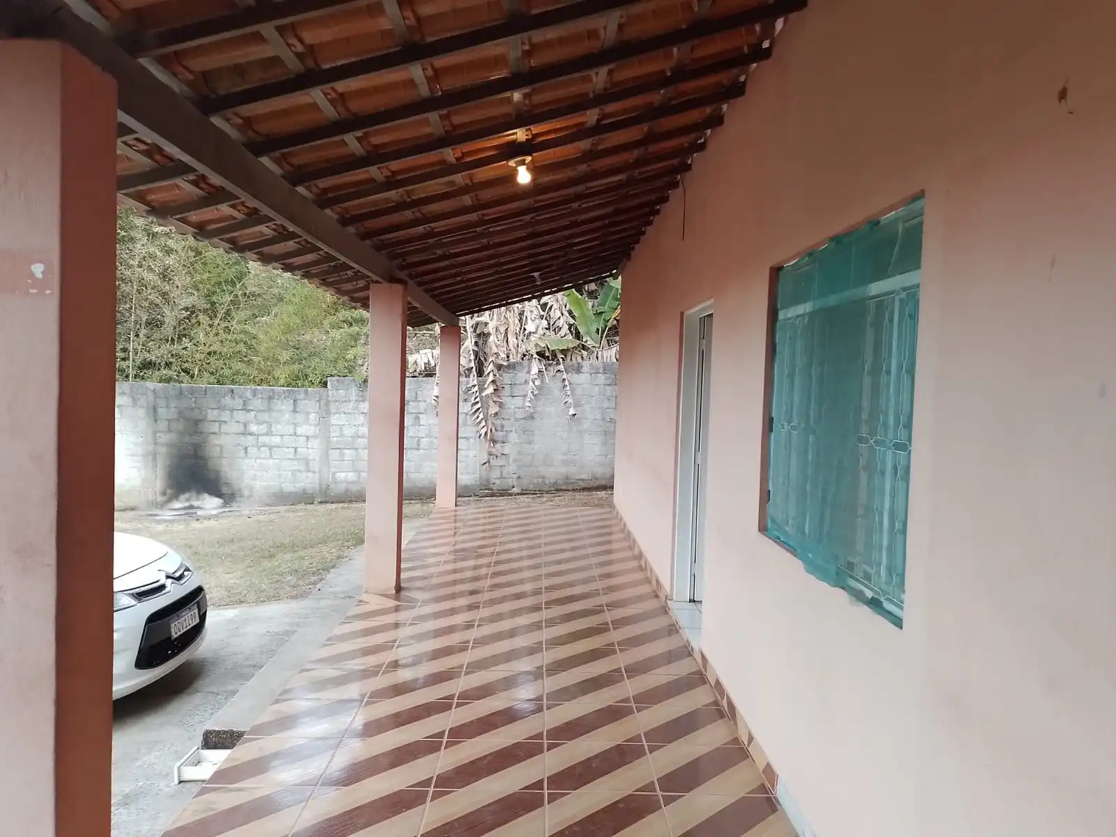 Varanda coberta com piso de ladrilho ao lado da área de estacionamento.