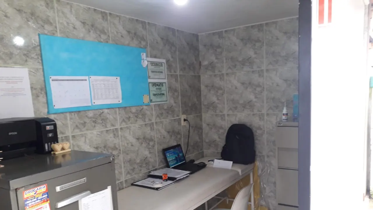 Sala de atendimento com mesa, computador e quadro de avisos.