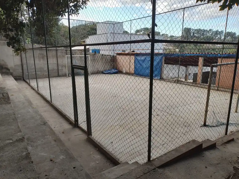 Quadra cercada por alambrado, com área gramada em volta.