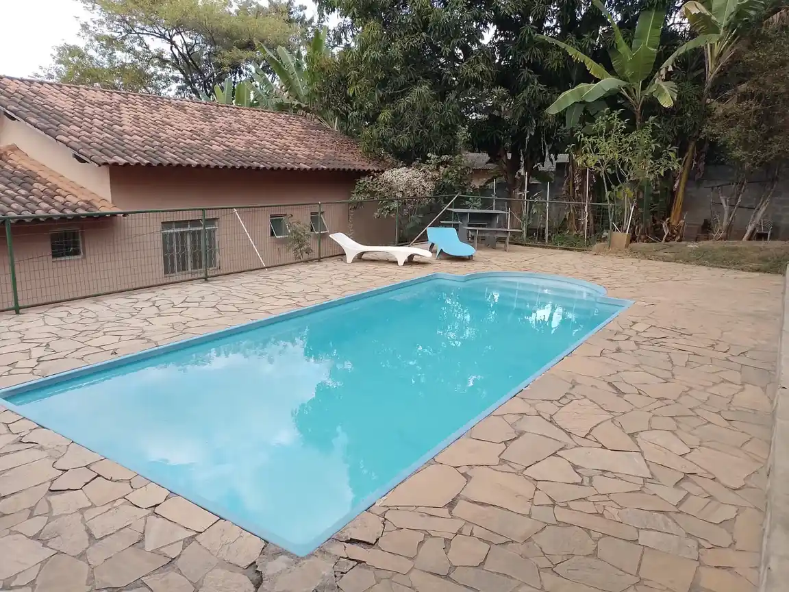 Piscina com deck de pedra e vegetação ao redor.